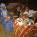 Standard Camp Merzouga Oasis featuring three people sitting around a small striped red and orange table with traditional Moroccan dishes and candles at night