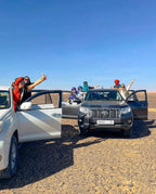 Sunset Desert Camps group enjoying outdoor adventure with white and gray 4x4 vehicles on rocky desert terrain under clear blue sky
