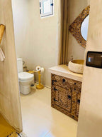 Sunset Desert Camps bathroom with beige walls, white toilet, wooden toilet paper holder, and decorative wooden vanity with a bowl sink