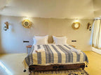 Sunset Desert Camps comfortable double bed with white pillows, patterned blanket, neutral walls, decorative round mirrors, and side lamps