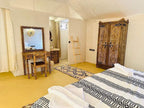 Desert camp interior at Sunset Desert Camps with beige canvas walls, yellow floor, patterned bedspread, and carved wooden furniture.