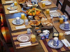 Breakfast table at Sunset Desert Camps with Moroccan ceramic plates, orange juice, bread, pastries, and fruit bowl on woven mats