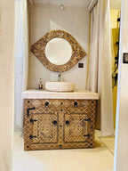 Sunset Desert Camps Moroccan bathroom featuring a rustic wooden vanity with intricate geometric patterns and a round mirror framed with natural wood slices