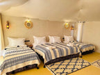 Sunset Desert Camps interior featuring three single beds with blue and white patterned blankets and rustic lantern lighting