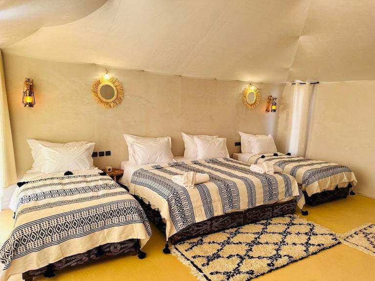 Sunset Desert Camps interior featuring three single beds with blue and white patterned blankets and rustic lantern lighting
