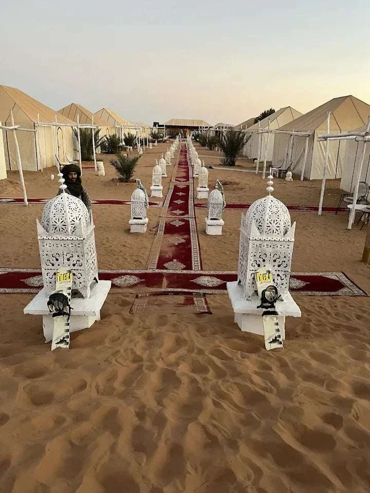 Sunset Desert Camps with white canvas tents and decorative lanterns lining a sandy path under a clear sky at dusk