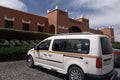 White taxi van with black and gold stripes, roof rack, and tinted windows parked in front of a terracotta hotel building, ideal for Taxi rent from Merzouga to Fes.