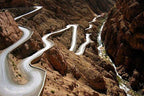 Winding mountain road with sharp curves carved into rocky brown terrain, illustrating a challenging route for Taxi rent from Merzouga to Fes.
