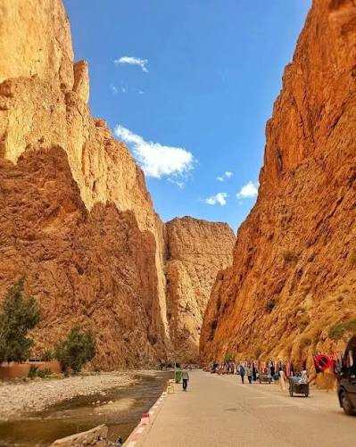 Scenic rocky canyon landscape with a paved road and small groups of people, illustrating the route for Taxi Rental from Merzouga to Ouarzazate.