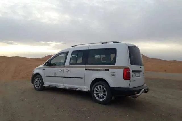 White multi-passenger van with tinted windows and roof rails parked on a desert road, perfect for Taxi Rental from Merzouga to Ouarzazate.
