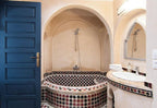 The Central House Marrakech Medina bathroom with arched beige walls, blue door, mosaic tiled bathtub, and curved sink countertop
