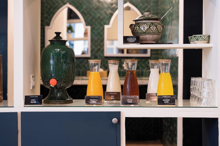 Beverage station at The Central House Marrakech Medina with glass dispensers containing pineapple juice, soy milk, apple juice, and orange juice in clear glasses