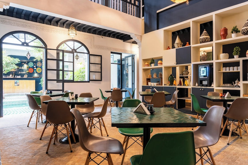 The Central House Marrakech Medina interior featuring multiple green and brown chairs around black tables with decorative wall shelves and patterned floor