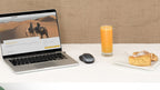 Laptop displaying Moroccan desert tour website, wireless mouse, glass of orange juice, and plate with cake and pastry on white table
