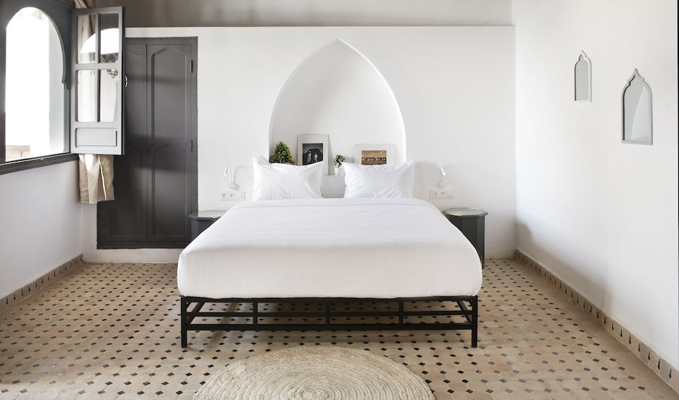 The Central House Marrakech Medina white minimalist bed room with arched niche wall, tiled floor, and black metal bed frame