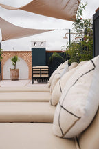 Outdoor seating area with beige cushions and striped pillows under white shade sails at The Central House Marrakech Medina