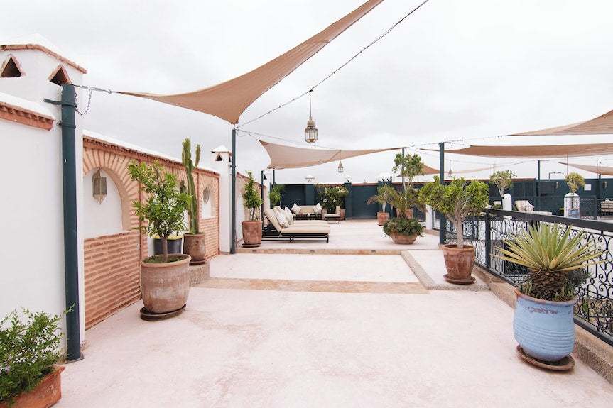 Outdoor terrace at The Central House Marrakech Medina with terracotta pots, green plants, beige sun sails, and lounge seating