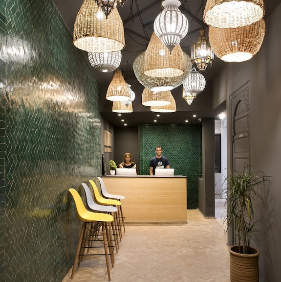 Reception area at The Central House Marrakech Medina featuring green tiled walls, wooden desk, modern chairs, and woven hanging lamps