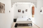 Minimalist white bedroom with a double bed, black metal frame, decorative arch, Moroccan style photos, and The Central House Marrakech Medina