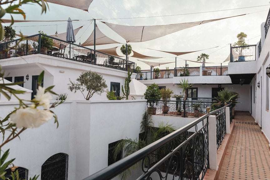 The Central House Marrakech Medina showcasing white stucco walls, terracotta tiled floors, black wrought iron railings, shaded outdoor terraces, and potted greenery