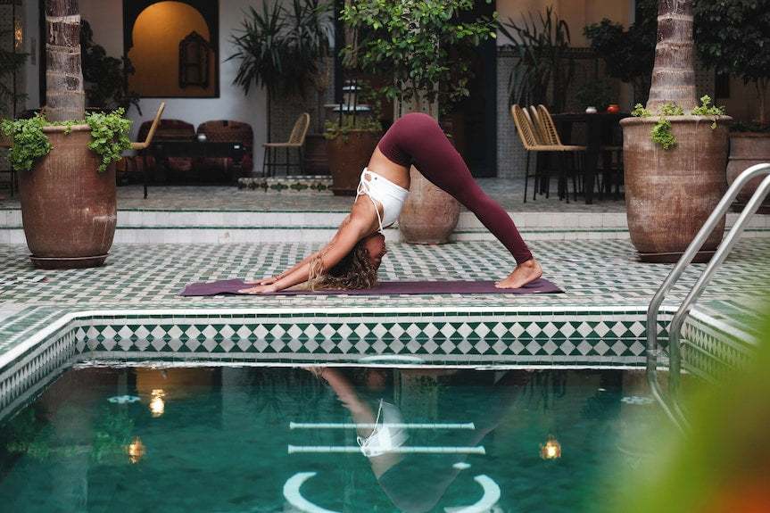 Yoga session by a decorated tiled poolside with geometric patterns and large terracotta pots at The Central House Marrakech Medina