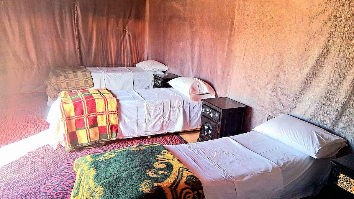 Tigmi Standard Desert Camp interior with three single beds featuring white linens and colorful patterned blankets