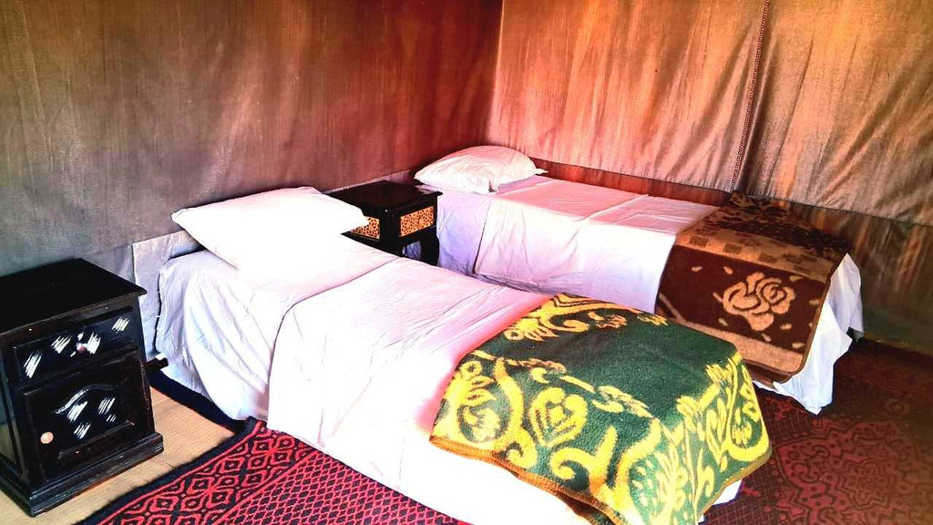 Tigmi Standard Desert Camp interior with two single beds featuring patterned blankets and white linens inside a fabric tent