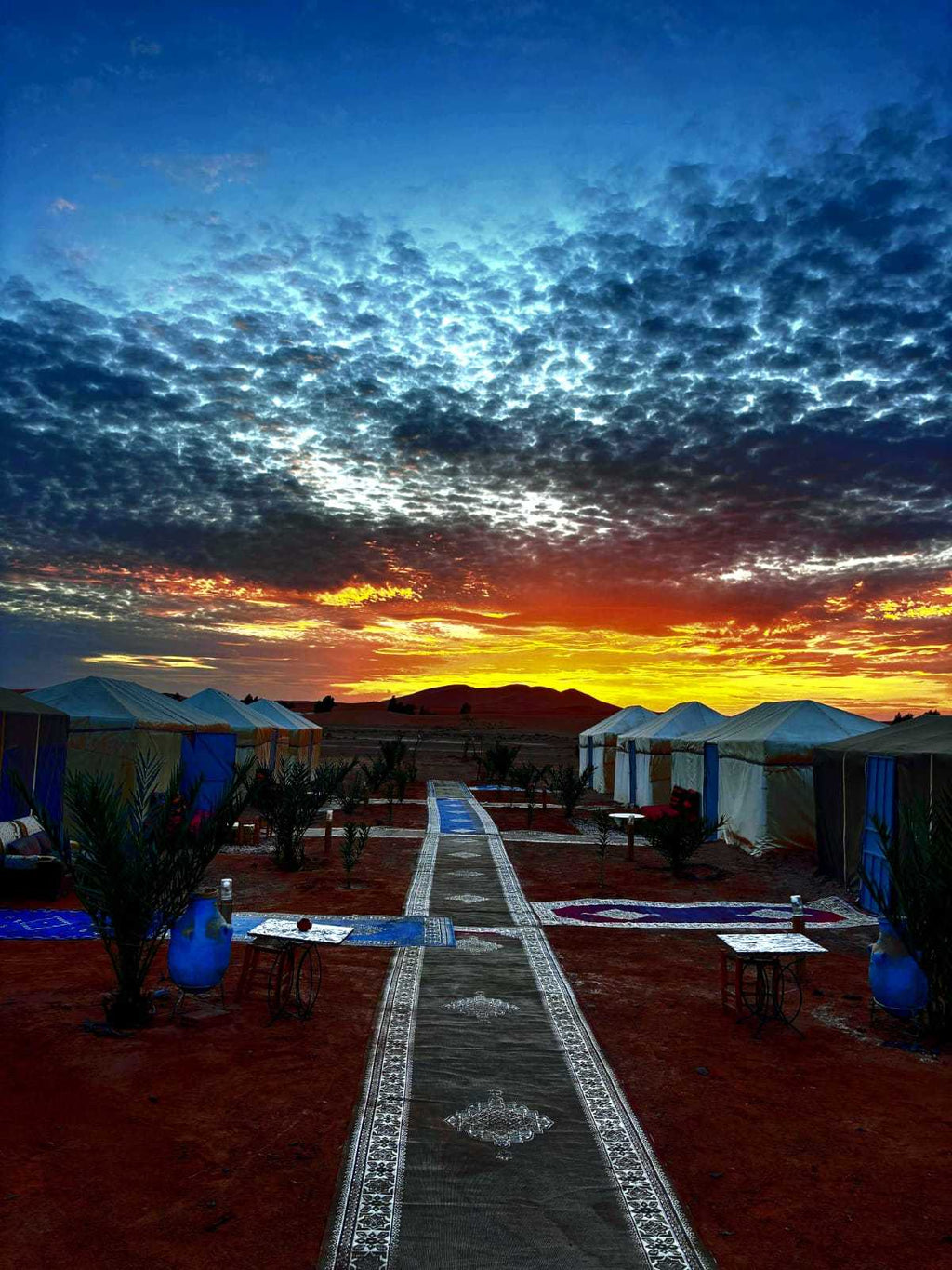 Tigmi Standard Desert Camp with white canvas tents and blue accents under a dramatic blue and orange sunset sky