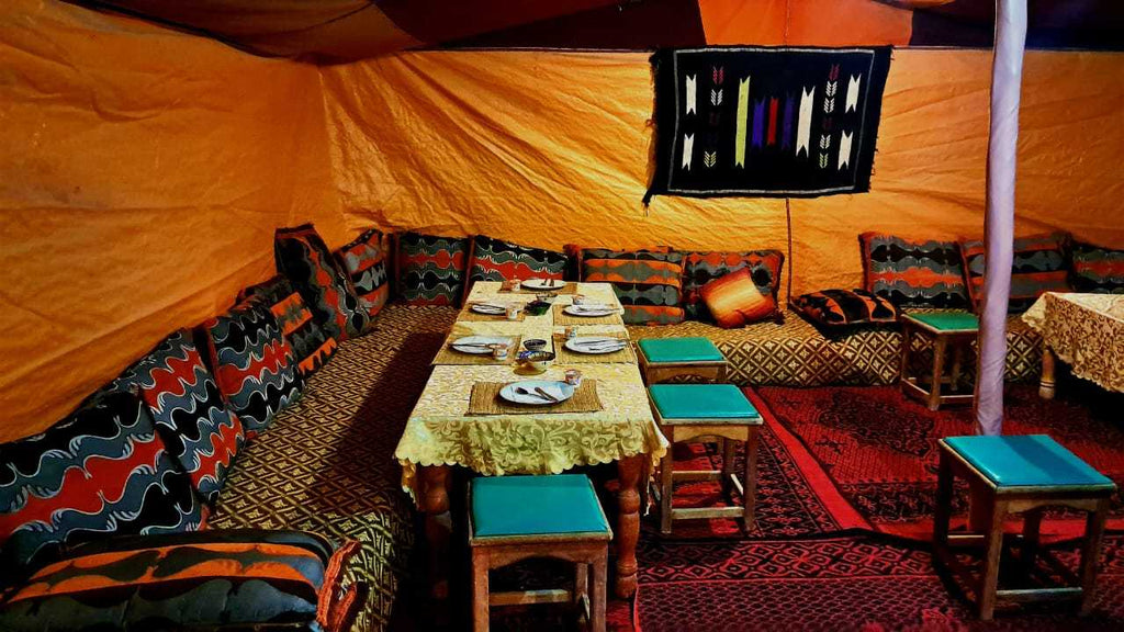 Tigmi Standard Desert Camp interior with yellow fabric walls, patterned cushions, small stools with turquoise seats, and a table set for dining
