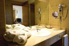 Bathroom countertop with beige tiles, white sink, wall-mounted magnifying mirror, hairdryer, and folded white bathrobes at Timoulay Hotel & Spa Agadir