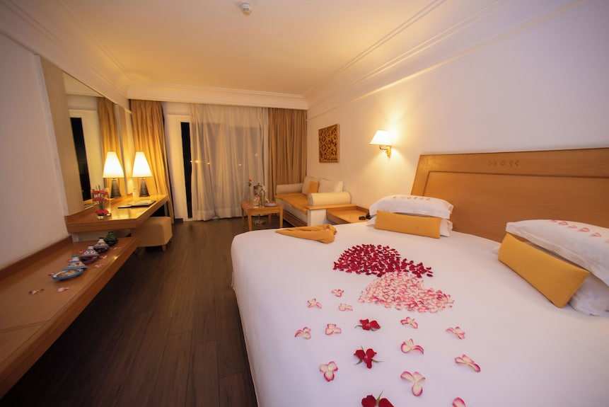 Timoulay Hotel & Spa Agadir spacious bedroom with wooden furniture, large bed adorned with rose petals, warm lighting, and a small sitting area