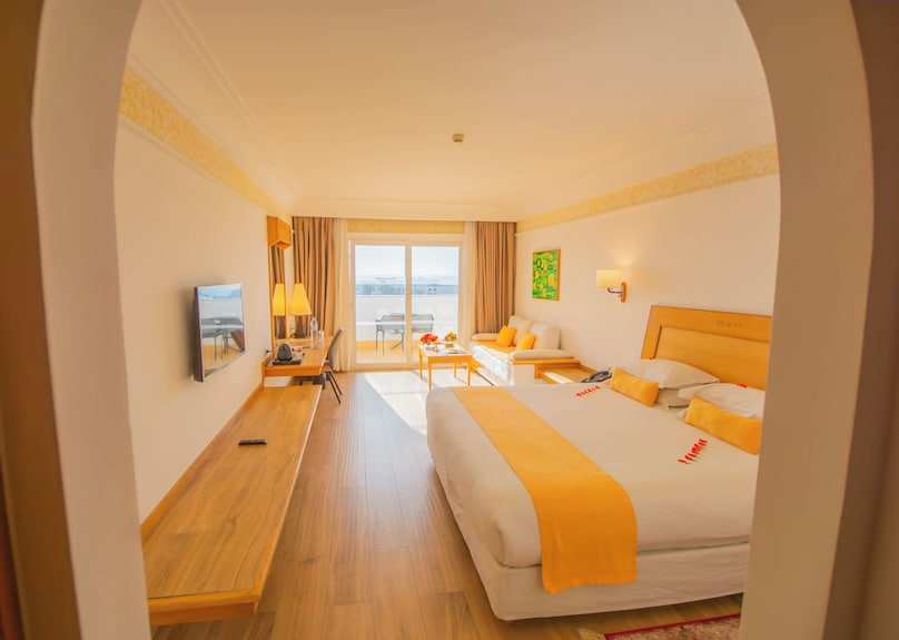 Hotel room at Timoulay Hotel & Spa Agadir featuring a large bed with yellow accents, wooden furniture, sofa, and balcony with city views
