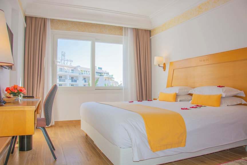 Hotel bedroom in Timoulay Hotel & Spa Agadir with white bedding, yellow accents, wooden furniture, and a city view window