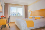 Hotel bedroom in Timoulay Hotel & Spa Agadir with white bedding, yellow accents, wooden furniture, and a city view window