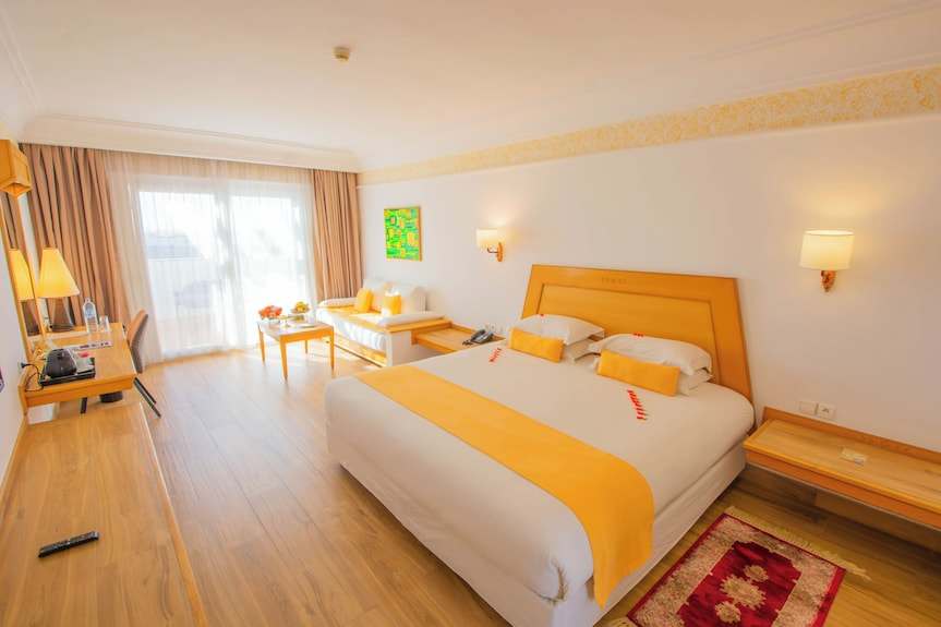 Timoulay Hotel & Spa Agadir bright hotel room with wooden flooring, white walls, yellow accents, king bed, sofa, and large window