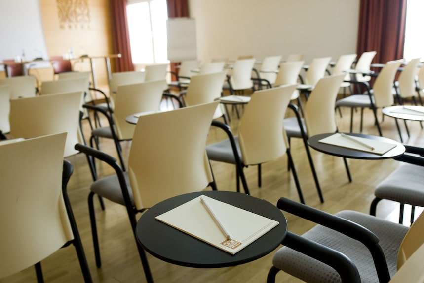 Conference room at Timoulay Hotel & Spa Agadir with beige plastic chairs, black armrests, and black round writing desks with notepads and pencils