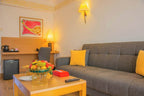 Hotel room at Timoulay Hotel & Spa Agadir with grey sofa, yellow cushions, wooden table with fruit basket, desk with chair and lamp