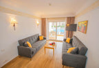 Hotel living room with two grey sofas, yellow accent pillows, wooden floor, wall lamps, and a balcony overlooking a pool at Timoulay Hotel & Spa Agadir