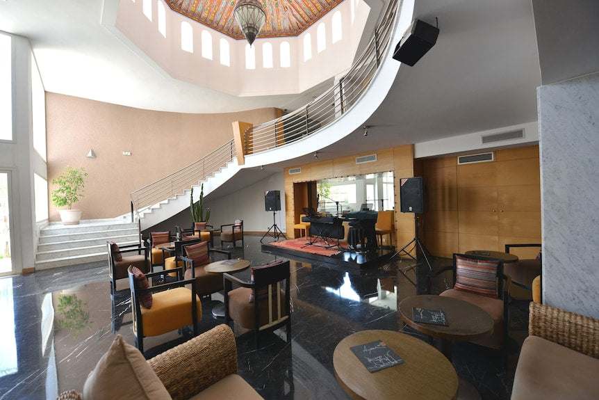 Lobby seating area with modern chairs, wooden tables, black marble floor, curved staircase, and colorful Moroccan-style ceiling at Timoulay Hotel & Spa Agadir