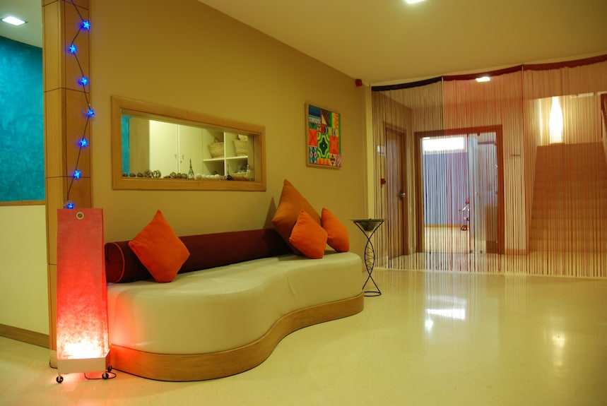 Lobby seating area with curved white sofa, orange cushions, beige walls, and decorative lamp at Timoulay Hotel & Spa Agadir