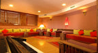 Lounge area with large U-shaped orange and green cushioned seating, wooden tables, Moroccan style rugs, and decorative lighting at Timoulay Hotel & Spa Agadir