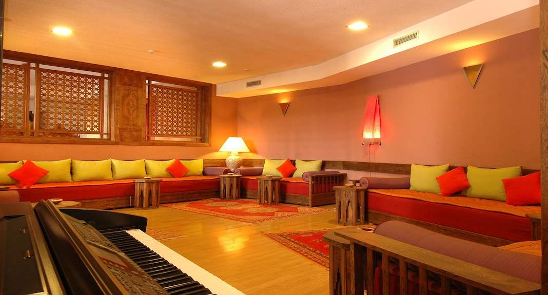 Lounge area with large U-shaped orange and green cushioned seating, wooden tables, Moroccan style rugs, and decorative lighting at Timoulay Hotel & Spa Agadir