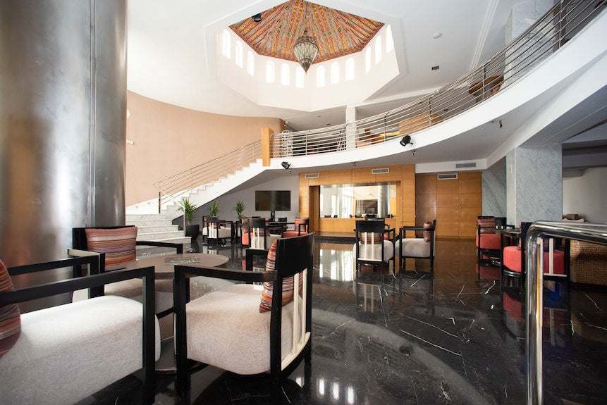 Spacious modern hotel lobby with black marble flooring, circular staircase, wooden accents, and Timoulay Hotel & Spa Agadir branding