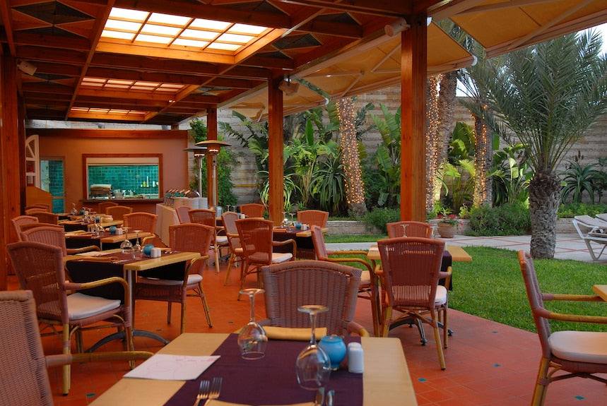 Outdoor dining area with wooden columns, wicker chairs, and tables under a wooden roof at Timoulay Hotel & Spa Agadir