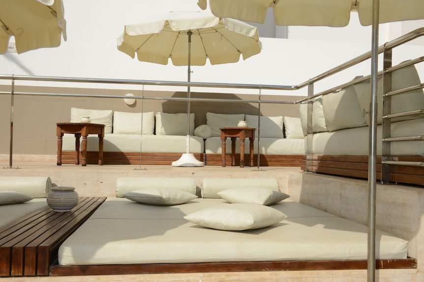 Outdoor lounge area at Timoulay Hotel & Spa Agadir featuring beige cushioned seating, wooden tables, and large cream umbrellas