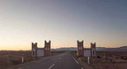 Road leading through traditional Moroccan desert gate structures with mountains in the distance during sunset on Tinghir to Merzouga journey