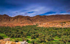 Scenic green palm-filled oasis and traditional village set against brown rocky mountains under a vibrant blue sky illustrating Tinghir to Merzouga journey