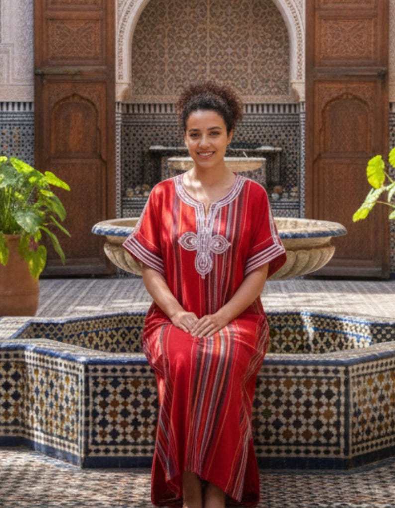 Red striped cotton traditional Moroccan kaftan with white silk embroidery on the neckline and sleeves worn by a seated woman.
