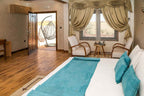 Yakout Merzouga Luxury Camp bedroom with white bed linens, turquoise cushions and runner, wooden floor, armchairs, and hanging chair outside
