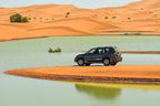 Yakout Merzouga Luxury Camp featuring a black SUV parked on orange sand surrounded by a blue-green desert lake and dunes